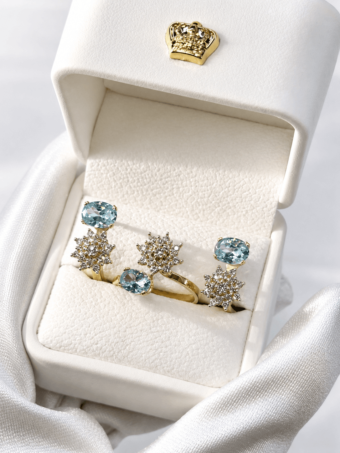 Three gold rings featuring blue gemstones and diamond starburst clusters in a white jewelry box.