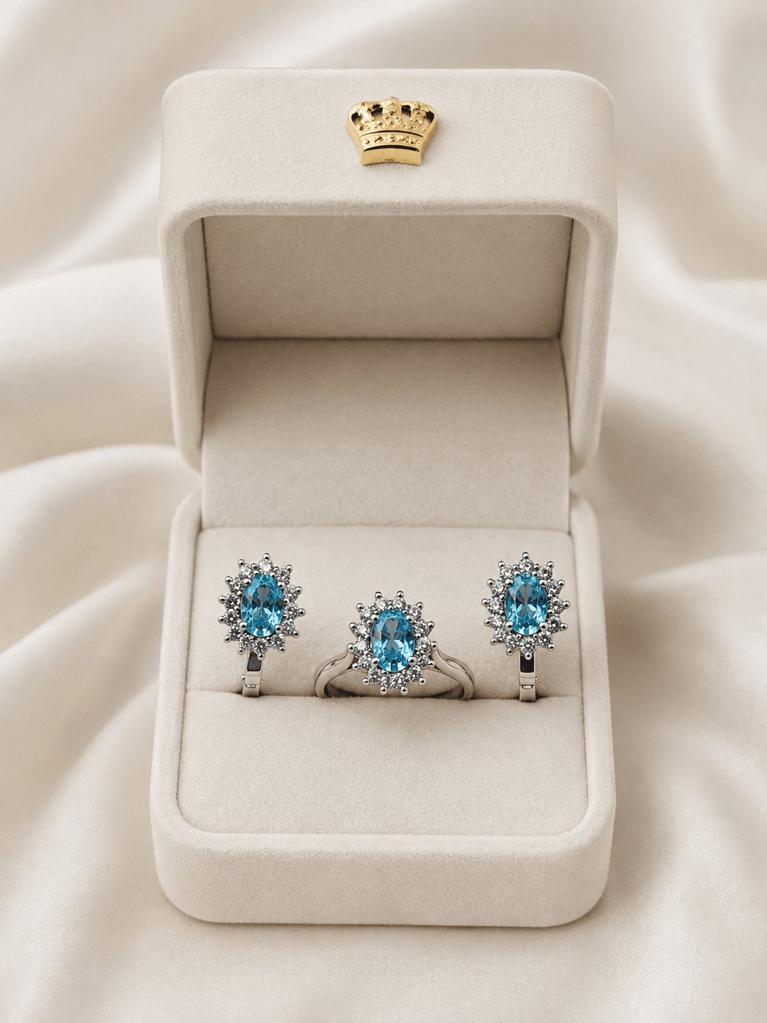 Blue gemstone jewelry set with diamond halos in a cream velvet box with gold crown.