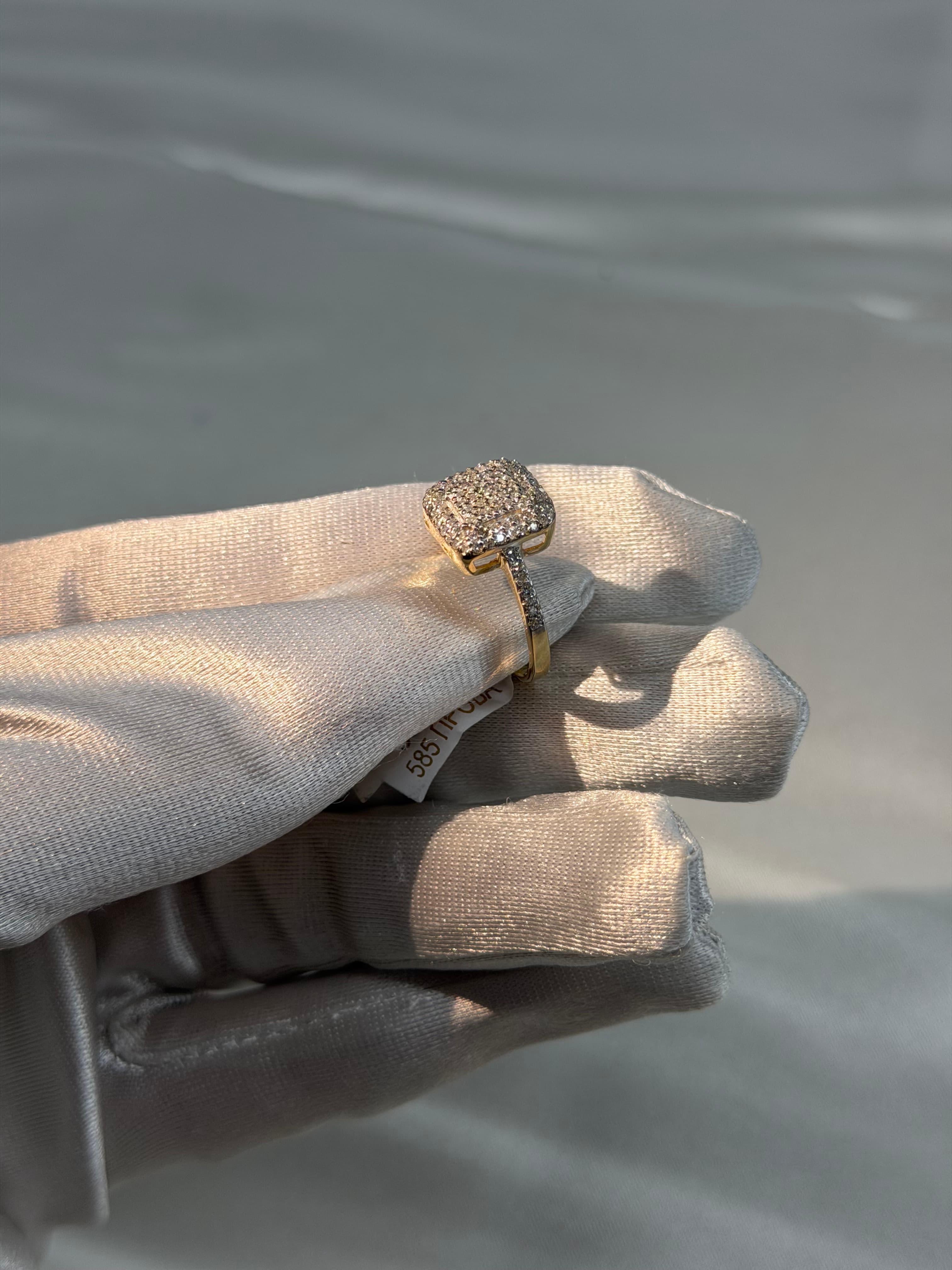 Square diamond cluster ring in gold held by a hand wearing a white satin glove.